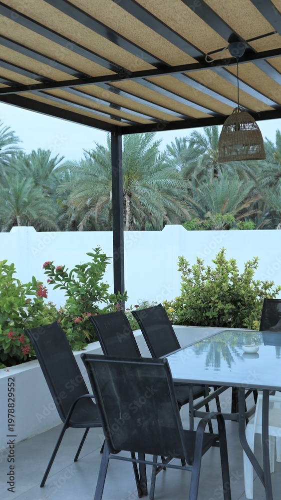 Fototapeta premium Outdoor Dining Setup. Comfortable Outdoor Area Perfect For Work Or Leisure Activities. Charming Shaded Patio With Stylish Furniture And Lush Greenery Creating Inviting Atmosphere