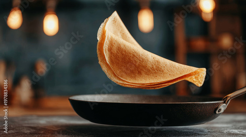 Pancake flipping in mid air over a dark frying pan during food preparation. Capturing motion and delicious homemade breakfast
