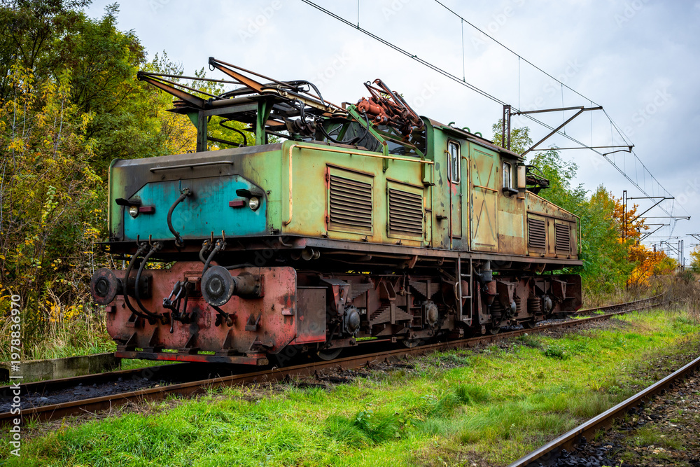 Obraz premium An old, green, electric shunting locomotive standing on a side track. The photo was taken on a cloudy autumn day.