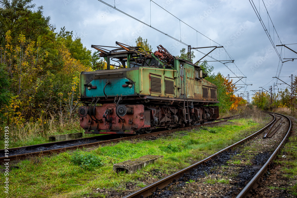 Obraz premium An old, green, electric shunting locomotive standing on a side track. The photo was taken on a cloudy autumn day.