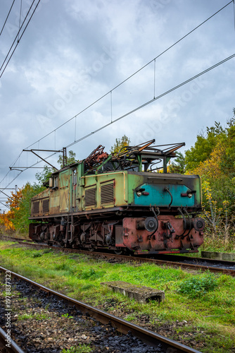 An old, green, electric shunting locomotive standing on a side track. The photo was taken on a cloudy autumn day.