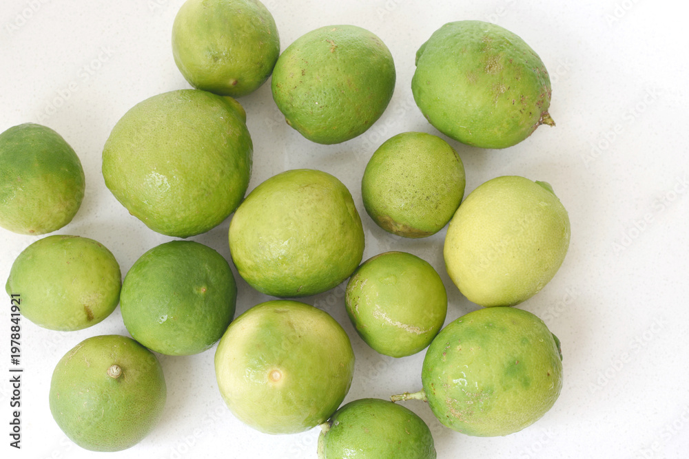 Fototapeta premium Top view of fresh green limes arranged on a clean white table, creating a bright and minimal citrus background. Ideal for concepts of freshness, healthy lifestyle, natural ingredients, summer drinks, 