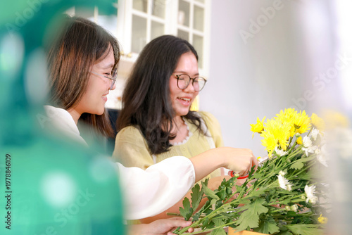 Two cheerful Asian teenage girls spend their free time arranging flowers in their kitchen decorate their home shared hobby among Gen Z friends helps them developflower arranging skills together.