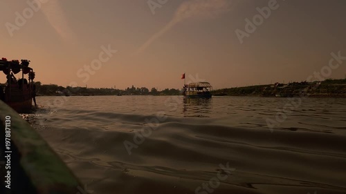 View from a moving boat showing gentle river waves and sunlight reflections. Calm natural scene with golden tones, ideal for travel, relaxation, background visuals, and nature footage.
