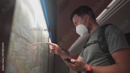 Allergy sufferer in a face mask looking at the timetable in Munich U-Bahn. Using a mobile app to navigate public transport during a strike day. Navigation bei Zugausfaellen in Deutschland