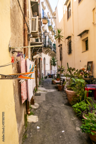 Narrow residential street in Palermo featuring rustic yellow-toned buildings, laundry hanging between balconies, and potted plants along the alleyway, capturing authentic local lifestyle