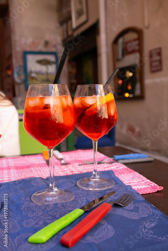 Two glasses of Aperol Spritz served over ice in large wine glasses within an Italian restaurant setting, showcasing the classic vibrant orange aperitivo cocktail and capturing a relaxed social dining 