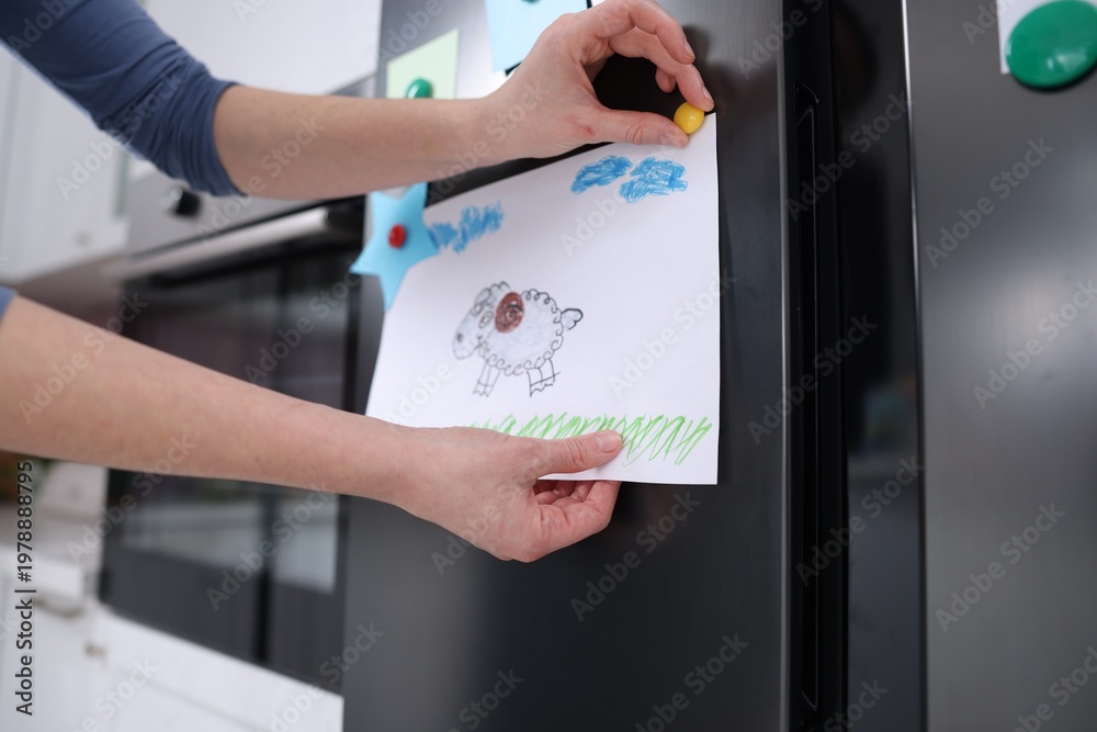 Naklejka premium Woman putting child's drawing onto refrigerator indoors, closeup