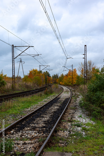 Electric traction above the tracks of an old railway line. High-voltage pylons in the background. Photo taken on a cloudy autumn day.