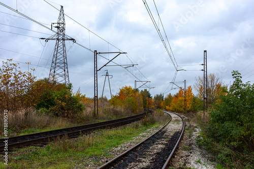 Electric traction above the tracks of an old railway line. High-voltage pylons in the background. Photo taken on a cloudy autumn day.