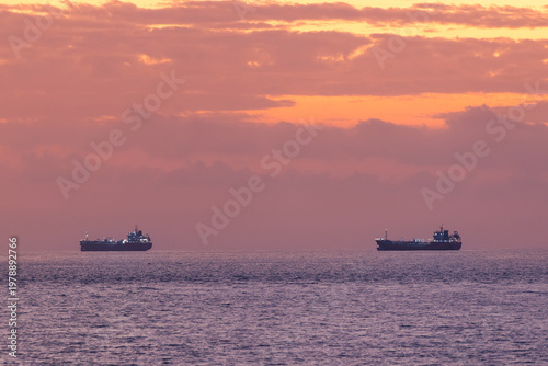фотографія Tanker ships with oil floating idle on calm ocean horizon at sunset, waiting for