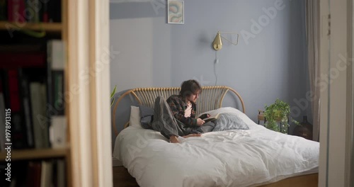 A peaceful morning unfolds with a person reading a book on a comfy bed, surrounded by sunlight and quiet vibes