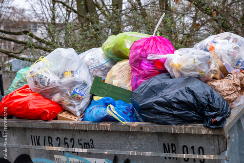 Overflowing metal dumpsters filled with plastic trash bags, outdoor waste disposal area, garbage collection point, municipal waste management, pollution nature, household waste disposal in Europe