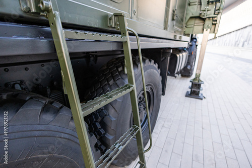 Military equipment and army equipment.. Closeup military truck ladder tires highlighting chassis details and tread texture, olive drab paint, urban pavement display conveying inspection