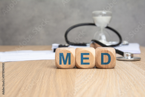 MED word in blue on wooden blocks. Blurred medical background with stethoscope and hourglass. Healthcare and medicine concept.