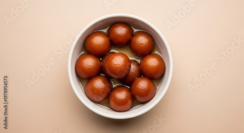 Top-down view of authentic Indian Gulab Jamun sweets, featuring golden-brown fried milk solid balls soaked in a translucent cardamom-infused sugar syrup, neatly arranged in a minimalist white ceramic 