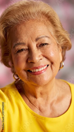 A portrait of a smiling mature woman with blonde hair wearing a bright yellow shirt