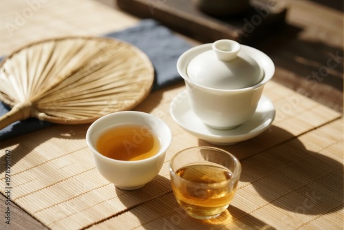 Traditional tea set with teapot, cups, and bamboo fan on a wooden table
