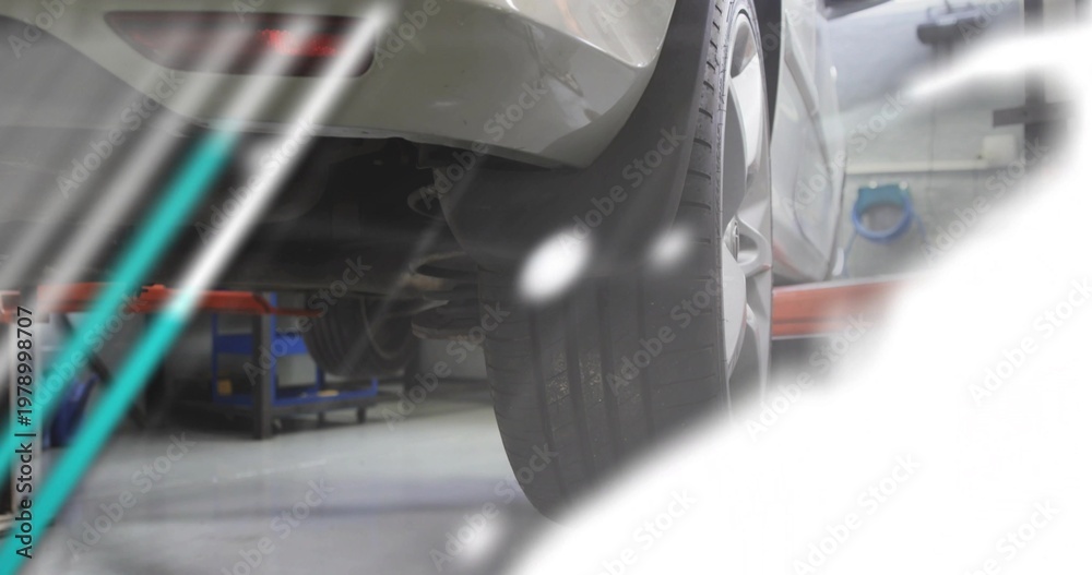 Fototapeta premium Showing rear-right tire and coil spring mounting on silver car in garage, with red lift arm