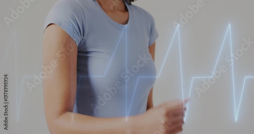 Showing mid adult woman wearing light blue tee moving arm in studio, with EKG waveform overlay