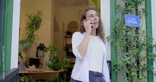 Nonbinary African American shop owner seeing message on pink phone, calling and waving by OPEN sign