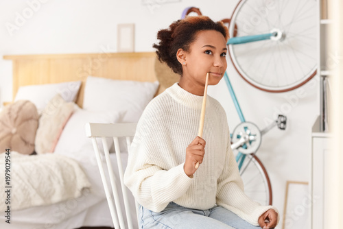 Thoughtful teenage African-American girl painting in bedroom