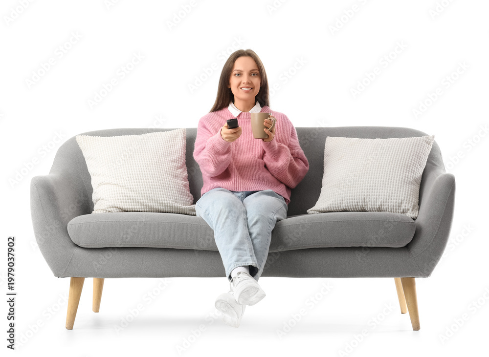 Obraz premium Young woman with cup of tea watching TV on grey couch against white background