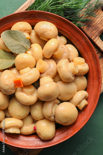 Bowl with tasty canned mushrooms, bay leaves and dill on green background, closeup