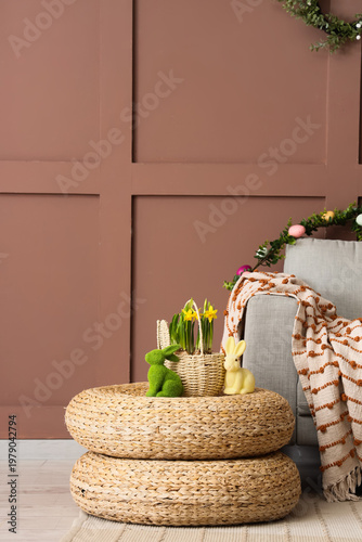 Basket with flowers and Easter rabbits on poufs near brown wall in living room