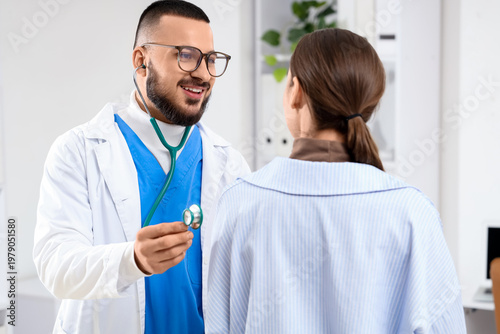 Male doctor with stethoscope listening to patient in clinic