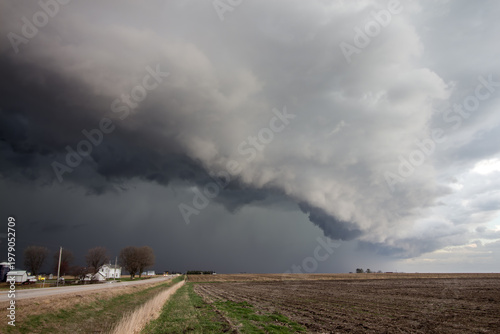 A dark storm approaches over rural farmland.