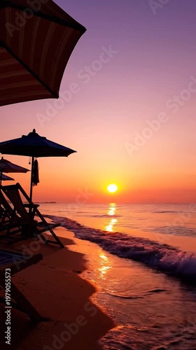 A peaceful tropical beach scene featuring empty lounge chairs and colorful umbrellas during a vibrant golden sunset over the ocean