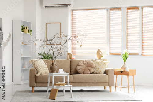 Interior of festive living room with grey sofa and tree branches decorated with Easter eggs on coffee table