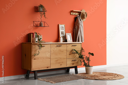 Tableau sur toile Wooden chest of drawers and houseplants near orange wall in interior of living r