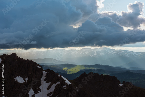 Dramatic aerial view above black sharp rocky ridge to sunlit green meadow amo...