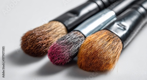 Close-up of three makeup brushes with varied colored bristles and black handles