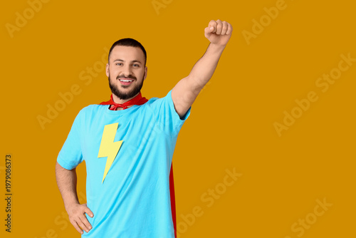 Young man dressed as superhero on orange background