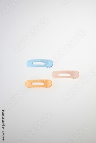 Three pastel hair clips rest against a clean white background. Soft hues include blue, peach, orange. Minimalist design suits modern fashion trends. Ideal for beauty, lifestyle, minimalist composition