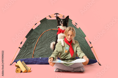 Valokuva Boy scout with cute Border Collie dog, map and tent sitting on pink background
