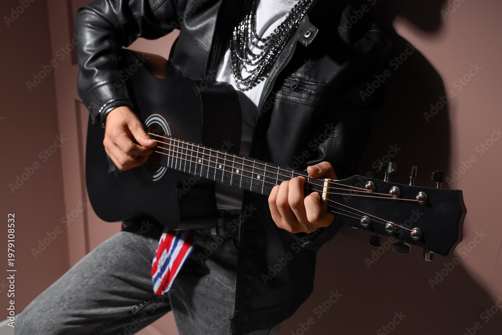 Obraz premium Young man in leather jacket playing guitar on brown background