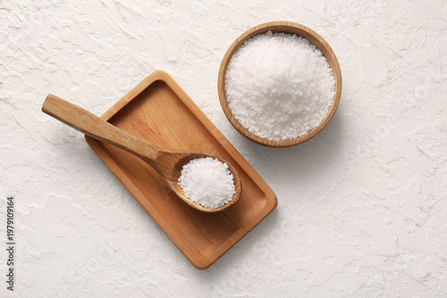 Wooden bowl of sea salt, spoon and board on light background