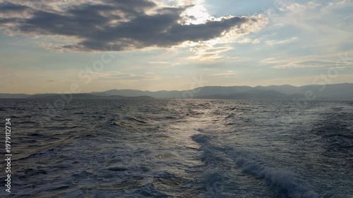 Cinematic view of rolling ocean waves under a dramatic sky with sunlit clouds. Scenic horizon with distant mountains and sea foam, perfect for travel and maritime visual projects.
