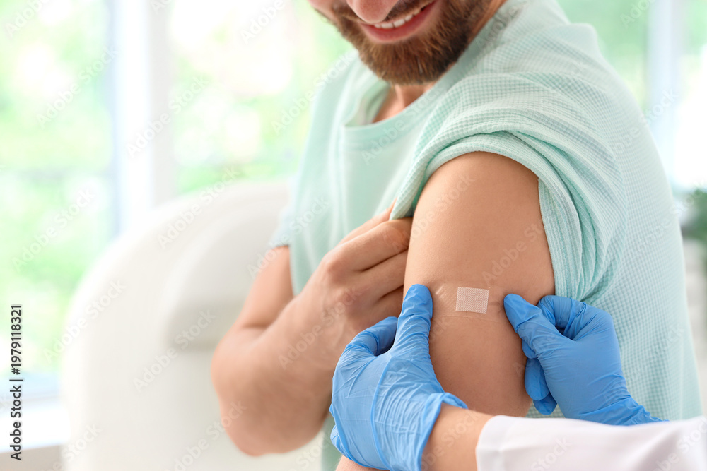 Obraz premium Young man receiving medical patch from doctor after vaccination in clinic, closeup