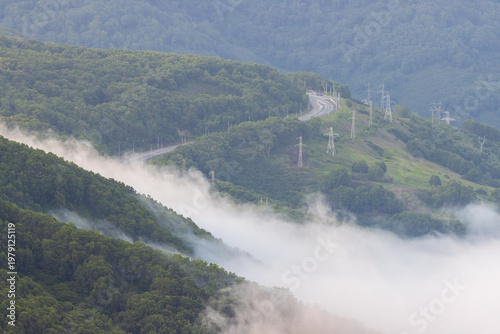 Mountain misty landscape. Fog and low clouds in the mountains. Top view of the clouds. Beautiful aerial photograph of the hills. Road and power line in the mountains. Kamchatka, Far East of Russia.