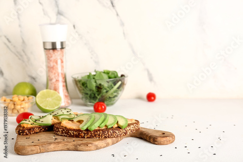 Tasty sandwiches with hummus, cucumber, avocado and ingredients on light table