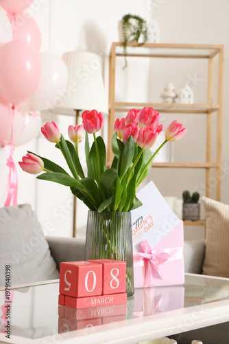 Vase with tulips, greeting card for Women's Day and cube calendar on table in living room