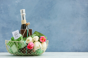 Basket with champagne bottle, tulips and chocolate for Mother's Day on table against blue grunge background