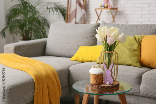 Glass coffee table with Easter cake, bunny and tulip flowers in festive living room, closeup