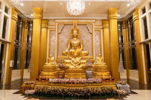 Obraz na płótnie A golden Buddha shrine fills the hall with seated statues and flower rows
