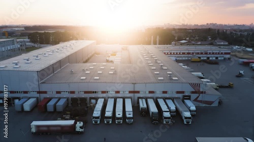 Aerial View of Large Logistics Hub and Warehouse Distribution Center at Sunset | Rows of Semi-Trucks at Loading Docks | Global Supply Chain and Freight Transportation Concept